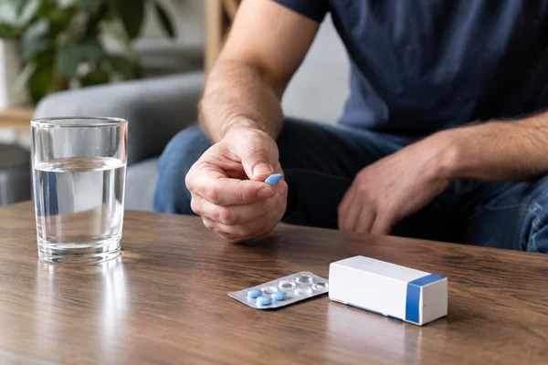 Man holding an ED medication tablet beside a glass of water.